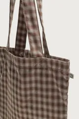 Bolso tipo shopper de la colección Benito Antonio x Zara, confeccionado en tejido con estampado a cuadros en tonos marrones y blancos. Cuenta con compartimento principal sin cierre, doble asa de mano y un pequeño bordado distintivo en la parte inferior.