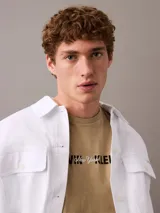 Remera de algodón con cuello redondo y manga corta, color beige. Presenta un estampado frontal con el logo de Calvin Klein y la inscripción New York en estilo cursivo.