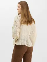 Cardigan abierto estilo kimono, color crudo, con mangas amplias al codo. Presenta una base con textura y motivos florales bordados a tono, con paneles de encaje calado estilo macramé en el frente, puños y ruedo.