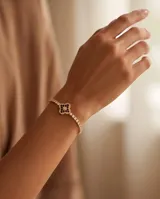 Pulsera de acero con baño dorado, compuesta por una cadena de circonias cúbicas y un dije central en forma de trébol decorado con circonias negras y blancas.