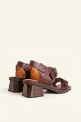 Sandalias de cuero negro con taco bloque de madera tallada, tiras con hebillas grandes y punta cuadrada.