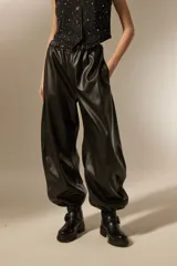 Babucha de cuero sintético color negro, con cintura elástica y puños ajustados en los tobillos. Presenta un diseño holgado y moderno con costuras horizontales en las piernas.