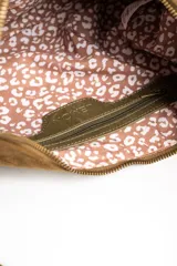 Cartera de hombro con diseño de flecos largos en la parte frontal, confeccionada en material sintético con textura de gamuza. Cuenta con una correa larga ajustable y cierre superior.