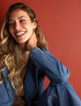 Chaqueta larga de jean azul con cuello con solapa, abertura central con botones, bolsillos delanteros, cintura con pasadores y lazo de ajuste, y puños con botón.