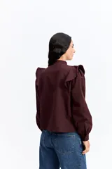 Camisa de color bordó con cuello mao y cierre frontal de botones. Presenta volados en los hombros que aportan volumen y un diseño sofisticado.