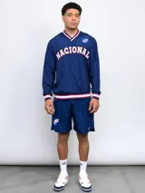 Buzo deportivo azul marino de nylon con cuello en V, puños y cintura acanalados con detalles tricolor (blanco, rojo y azul). Estampado frontal con la palabra "NACIONAL" en blanco y escudo del club C.N.de F. en el pecho. Corte clásico.