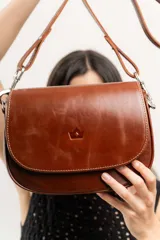Cartera bandolera de estructura firme, confeccionada en cuero natural con solapa y cierre magnético, e incluye correa larga ajustable.