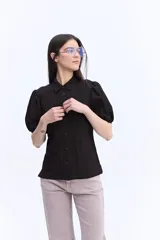 Camisa negra de manga corta abullonada, con cuello clásico y cierre frontal de botones.