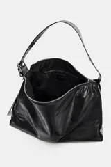 Bolso tipo saca de gran tamaño, color negro, con asa de hombro ajustable decorada con ojales metálicos y cierre principal mediante cremallera.