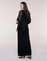 Vestido largo azul marino de seda fría, compuesto por una falda recta con tajo frontal y una capa superior superpuesta de encaje con lentejuelas bordadas, escote a la base y mangas tres cuartos acampanadas.