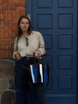 Matera de cuero con diseño de paneles verticales en combinación de colores azul, verde, marrón y bordó. Cuenta con dos asas cortas de cuero y estructura rígida.