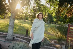 Triángulo de lana color beige con maxi flecos, diseñado por Margara Shaw en colaboración con Manos del Uruguay. Confeccionado con una mezcla de lana merino, mohair, viscosa, algodón y otras fibras, incluyendo lurex y un hilado teñido a mano con lentejuelas.