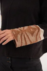 Polera de calce relajado con cuello alto, confeccionada en lana. Presenta un diseño bicolor con cuerpo en gris claro y mangas con estampado jacquard de arabescos en tonos tierra y negro. Incluye detalle de costura central vertical en el frente.