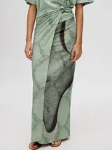 Pareo largo de viscosa en color verde menta, con diseño estampado que presenta gráficos abstractos y una figura central destacada en negro. Es una prenda liviana y fresca, ideal para usar sobre el traje de baño o como falda envolvente.