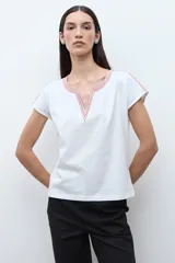 Remera blanca de algodón con escote en V y detalles de bordado étnico en tonos rojizos y naranjas en el cuello y los hombros. De corte recto y manga corta.