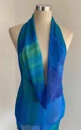 Vestido corto ajustado, sin mangas, con escote halter pronunciado y drapeado tipo cowl neck. Presenta un estampado abstracto en tonos azules y verdes que simulan olas o agua.