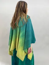Ruana de lana merino con diseño en degradé de tonos verdes. Presenta un cuello plisado artesanalmente en fieltro de lana merino, ofreciendo una textura suave y un acabado elegante.