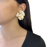Aros cortos con forma de flor tipo moño de lazo, hechos en resina color crema. Se ajustan con perforación y son livianos.