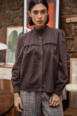 Camisa de broderie color chocolate, con cuello alto con volados, cierre frontal de botones y mangas largas con volumen.