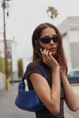 Bolso de hombro azul de diseño estructurado tipo hobo, con asa ajustable y cierre de cremallera con tirador. Cuenta con un bolsillo interior con cremallera.