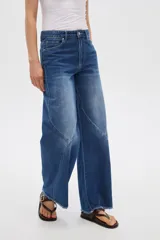 Pantalón jean gris de tiro alto, corte ancho (wide leg) con diseño de paneles tipo patchwork y terminación desmechada en el dobladillo.