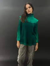 Buzo verde esmeralda de lana merino con cuello alto y mangas largas. Presenta dos texturas: afieltrada en cuello, mangas y ruedo, y tejido merino superfino en el delantero y la espalda.