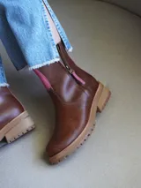 Botas cortas de cuero blanco con suela track marrón y detalles en gamuza beige en la parte frontal y trasera. Cuenta con cierre lateral y tirador de cuero.