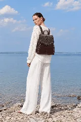 Mochila de cuero marrón con solapa superior en pico y textura símil reptil, cierres laterales y asas traseras.