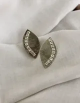 Par de aros colgantes con forma de hoja, hechos en alpaca color plateado y decorados con una hilera de strass.