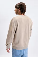 Buzo de polar color taupe con cuello redondo, puños y ruedo acanalados. Presenta una estampa sutil en el pecho con texto decorativo.