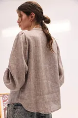 Blusa de lino color beige, de cuello redondo y manga larga abullonada. Cuenta con detalles de pliegues y ribetes oscuros en la pechera.