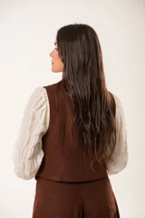 Chaleco marrón con escote en V, sin mangas y cierre frontal con botones.