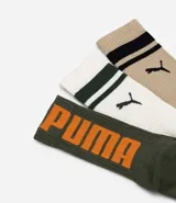 Kit de tres pares de medias deportivas Puma de caña larga. Un par es beige con dos rayas marrones y logo de Puma. Otro par es blanco liso. El tercer par es marrón oscuro con dos rayas blancas y logo de Puma. Todas están confeccionadas en algodón.