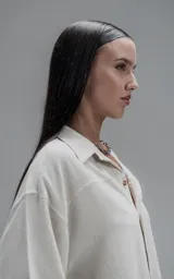 Camisa de corte oversize con cuello camisero, cierre frontal de botones y mangas cortas. Presenta un diseño holgado con bolsillos laterales integrados en la costura.