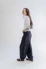 Pantalon de corte holgado y estilo bombacho, confeccionado en tela suave con ligero brillo. Presenta cintura elastizada en la parte trasera y puños elásticos en los tobillos que definen su silueta.