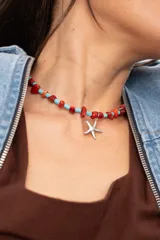 Gargantilla corta de cuentas turquesas tubulares y piedras rojas irregulares, con dije colgante de estrella de mar plateada.