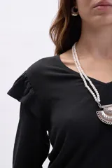 Blusa negra de manga larga con textura, cuello en V y detalle de volados en los hombros. Presenta mangas con puños elásticos y un corte recto.