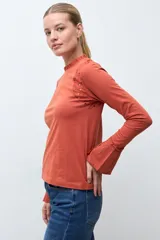 Remera de manga larga color terracota, con cuello alto y detalles de broderie en los hombros y puños acampanados.