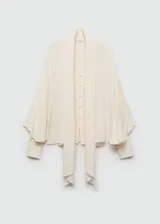 Blusa de tejido fluido en color crema, con diseño oversize, cuello en pico con lazo integrado, cierre frontal de botones y mangas largas con puños abotonados.