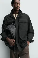Mochila de diseño minimalista en color negro, confeccionada en material sintético con acabado grabado. Cuenta con un compartimento principal con cierre de cremallera, un bolsillo frontal con cierre y un compartimento posterior acolchado para dispositivos electrónicos. Incluye asa de mano superior y dos correas de hombro ajustables.