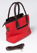 Cartera de mano roja de cuero sintético con doble asa corta marrón y correa larga marrón desmontable. Tiene dos compartimentos principales con cierre y bolsillos internos.