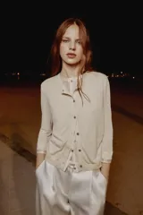 Chaqueta efecto doble de punto color beige con cuello redondo, manga por debajo del codo y cierre frontal con botones. Detalle de cuello y bajo de camisa interior asomados.