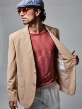 Saco color beige de piqué con cuello con solapas y bolsillos de plastrón. Mangas con coderas y bajo con abertura en espalda.