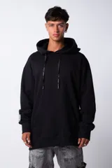 Buzo canguro oversize de tela friza, color negro, con capucha, cordones ajustables con logo y bolsillo frontal tipo canguro.