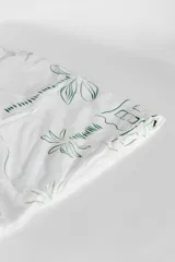 Pareo de playa blanco con estampado de hojas verdes y borde de encaje con flecos.