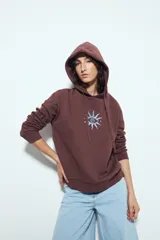 Canguro negro de calce relajado con capucha y cordones ajustables. Presenta un estampado gráfico frontal de un ojo con rayos de sol y la frase "STAY WEIRD".