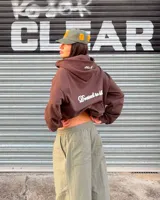 Campera con capucha y cierre frontal de Nude Project, color marrón, con corte boxy y diseño oversized. Presenta un parche bordado en relieve con las iniciales NP en el pecho, capucha amplia y bolsillos tipo canguro.