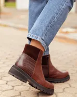 Botinetas de cuero color chocolate con diseño de paneles combinados en cuero liso y cuero texturizado. Presentan una suela track gruesa de goma negra y un corte tipo chelsea.