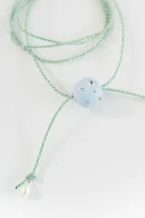 Gargantilla tipo bolo tie de tiento trenzado verde con dije esférico celeste con brillos incrustados.