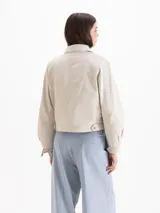 Campera bomber color beige, confeccionada en una mezcla de poliéster y algodón, con cuello camisero, cierre frontal con cremallera y volados superpuestos en la pechera.
